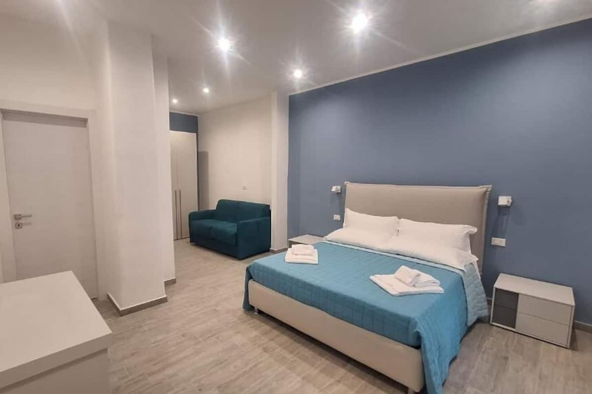 Una habitación de hotel moderna con una cama, una mesita de noche, una silla y una pequeña mesita auxiliar.