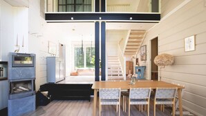 A modern kitchen with a dining area, featuring a wooden table and chairs, a built-in oven, and a staircase leading to an upper level. - Stay North - Västerskog (Sipoo)