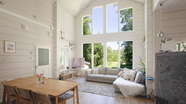 A spacious room with a wooden dining table, a sofa, and a large window offering a view of greenery. - Stay North - Västerskog (Sipoo)