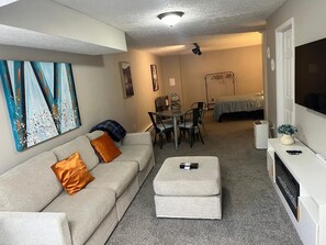 A living room with a sofa, ottoman, and a dining area with chairs and a table.