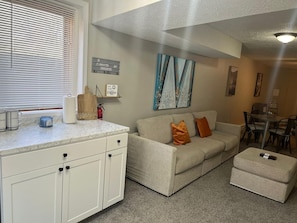 A living room with a sofa, ottoman, coffee table, and a dining area with chairs and a table.