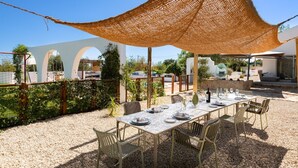 An outdoor dining area with a table set for four, surrounded by chairs, under a woven shade structure. - Holiday Home 'Modern Farmhouse with Pool' with Mountain View, Wi-Fi and Air Conditioning (Santo Estevão)