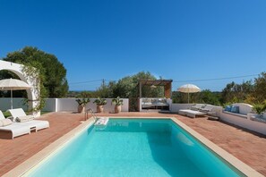 Une piscine rectangulaire entourée de chaises longues et de parasols, agrémentée de plantes en pot et d’une pergola.