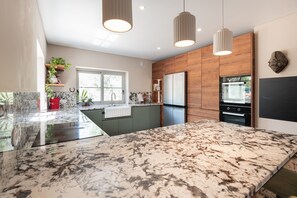Une cuisine moderne dotée d’un grand plan de travail en marbre, de meubles en bois, d’appareils électroménagers en acier inoxydable et de luminaires suspendus.
