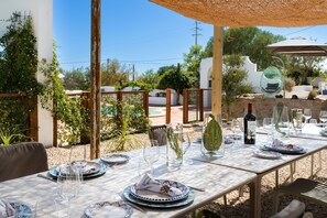 Un espace de restauration en plein air avec une table dressée pour un repas, entouré de verdure et d’une piscine.