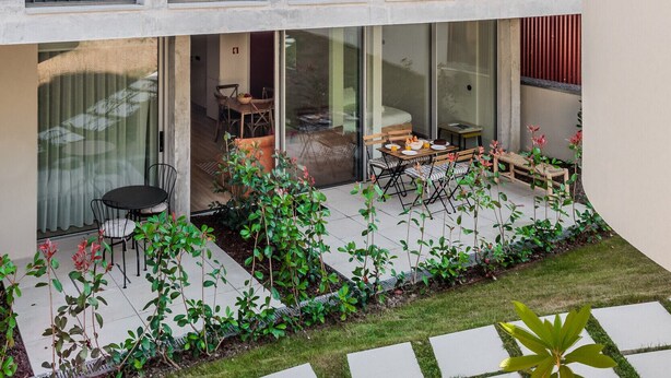 Ein modernes Gebäude mit mehreren Balkonen, einem Innenhof mit Sitzgelegenheiten und einem Gartenbereich.