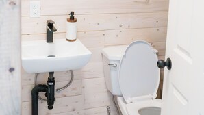 A small, wooden-paneled bathroom with a white sink, a toilet, and a mirror above the sink. - Salmon Bay Farm (Rivière-Saint-Paul)