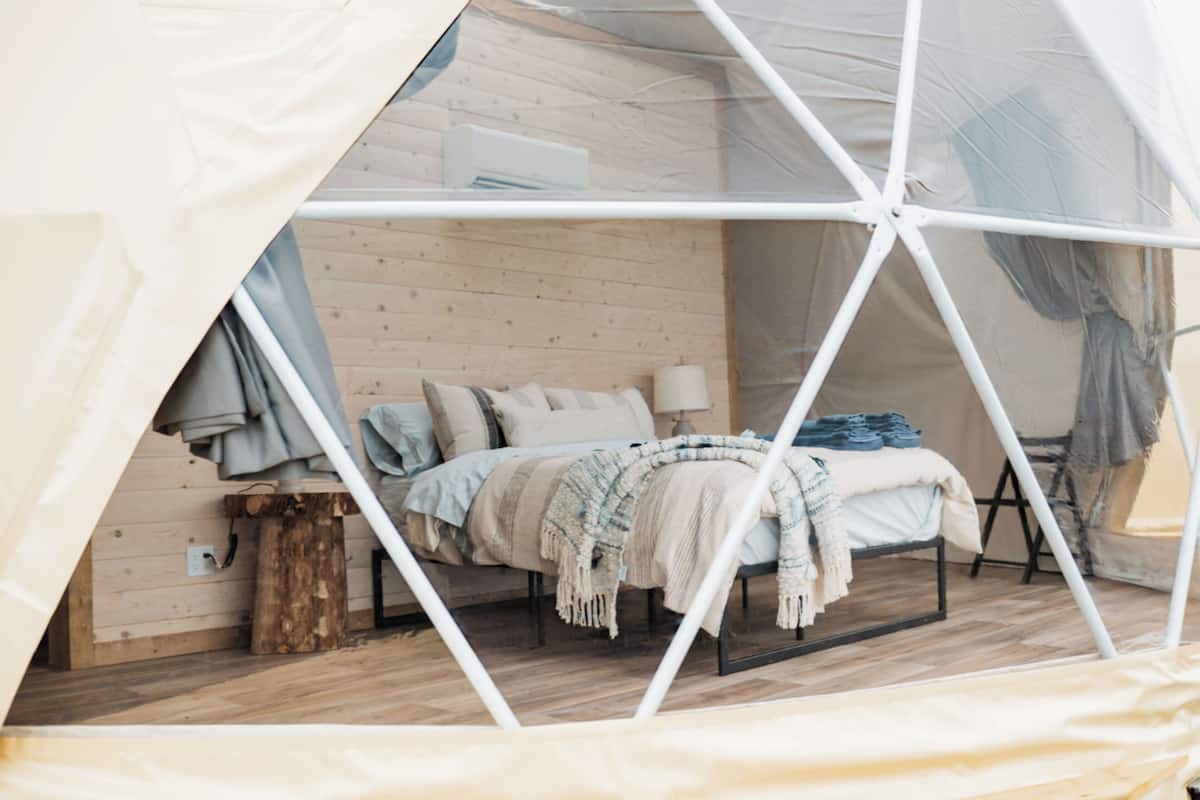 A tented room with a bed, wooden walls, and a window.