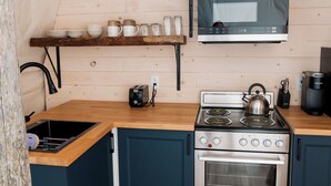 A kitchen with a wooden countertop, a stove, an oven, a microwave, and a shelf with kitchenware. - Salmon Bay Farm (Rivière-Saint-Paul)