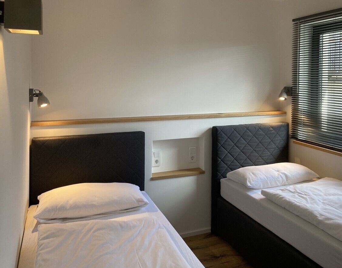 Ein kleines Zimmer mit zwei Betten, jeweils mit Kopfstütze und Nachttisch.