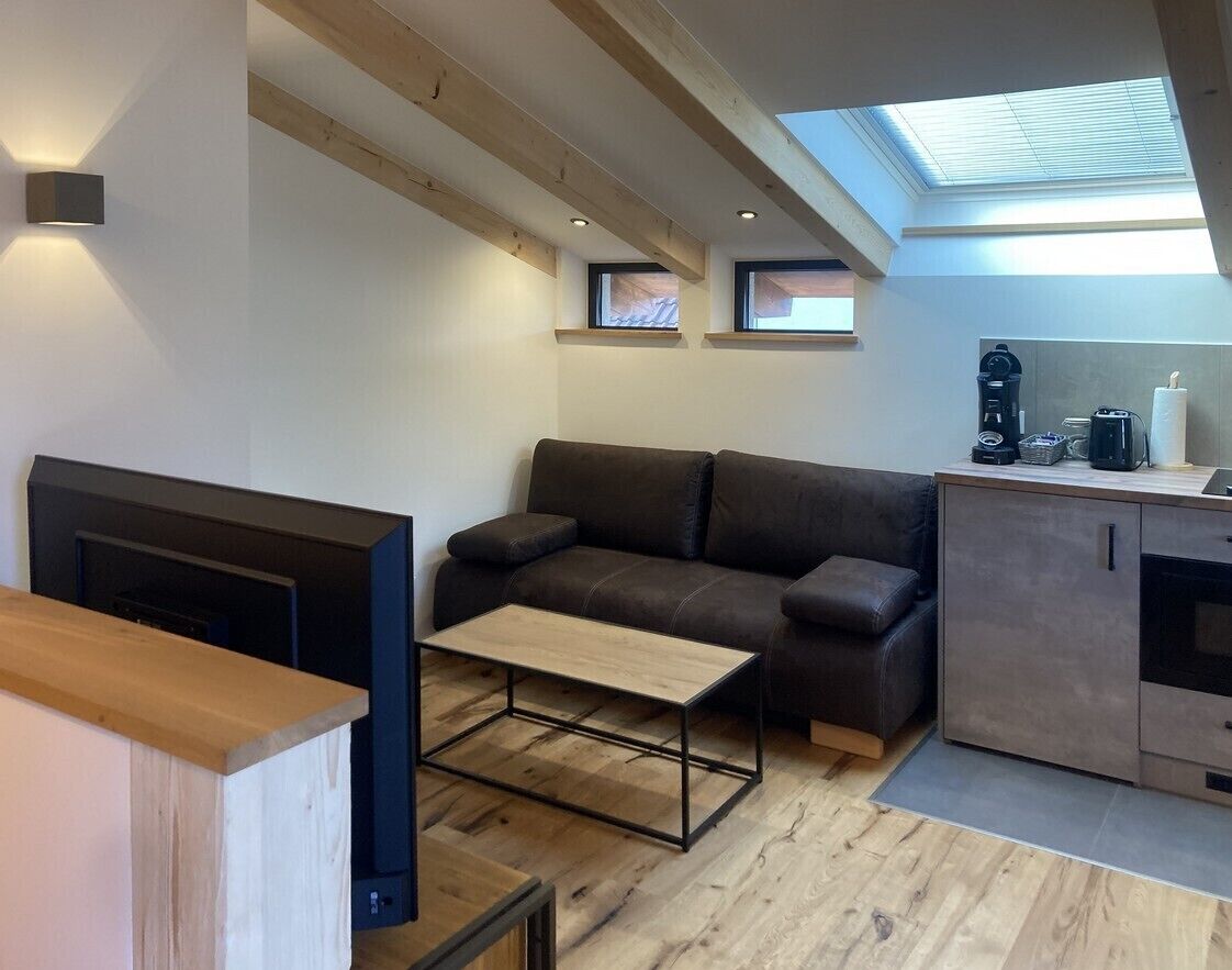 A compact living space with a sofa, a coffee table, a TV, and a kitchenette.