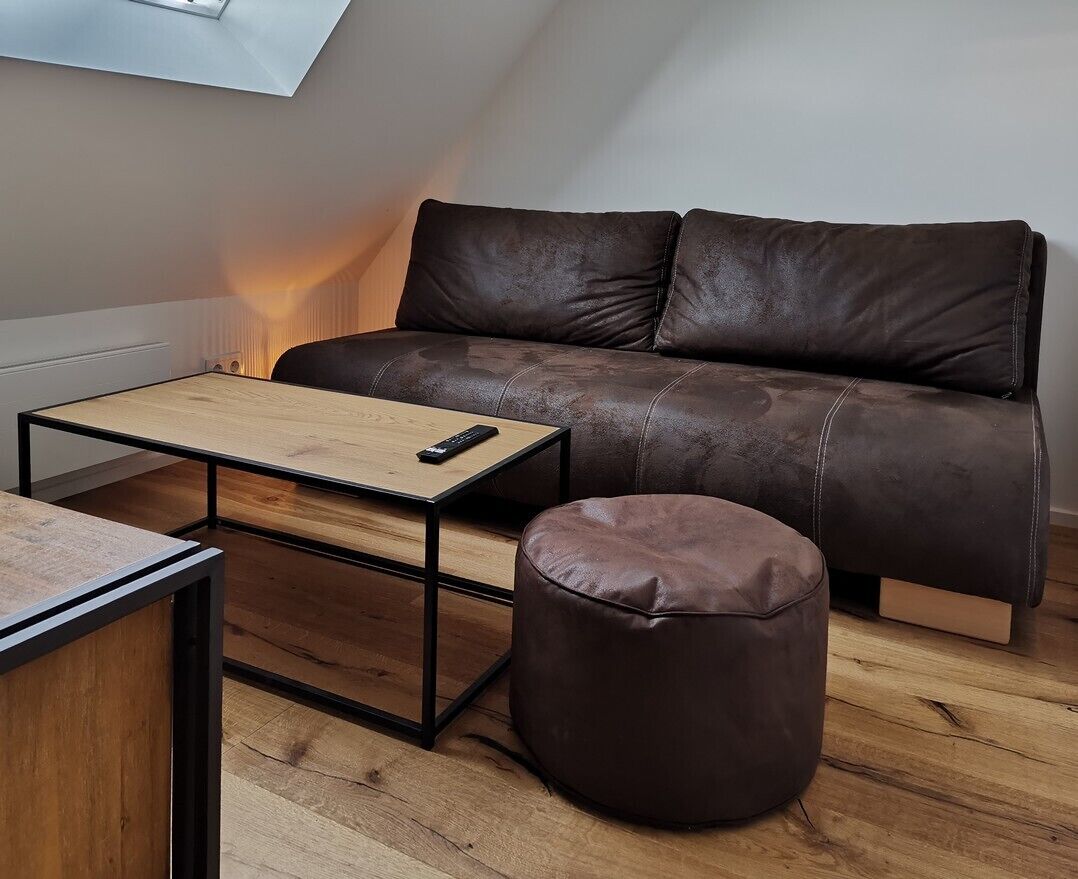 A modern living room with a brown leather sofa, a wooden coffee table, and a round ottoman.