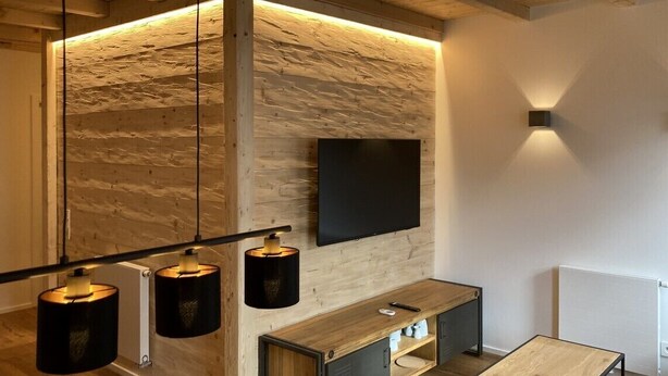 Una habitación moderna con una pared de madera, un televisor de pantalla plana, un banco de madera y lámparas colgantes.