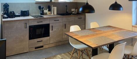Una cocina moderna con armarios de madera, horno empotrado, una mesa de comedor con sillas e iluminación colgante.
