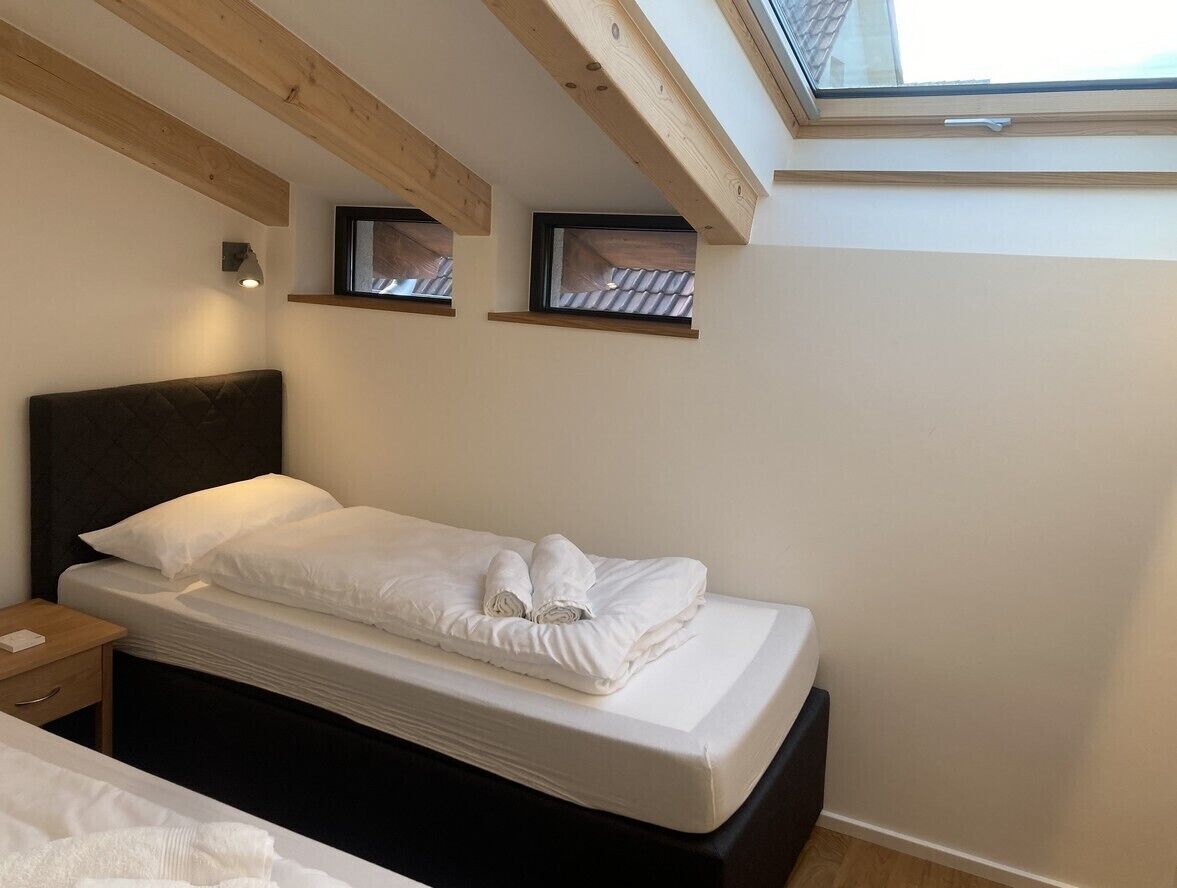 A bedroom with a bed, a nightstand, a skylight, and two framed pictures on the wall.