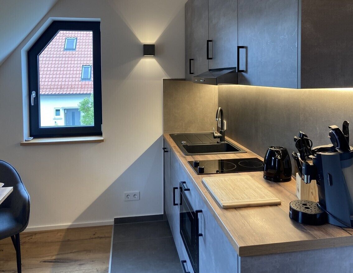 Una cocina moderna con estufa integrada, un lavamanos y un ventanal con vistas a un edificio de tejados rojos.