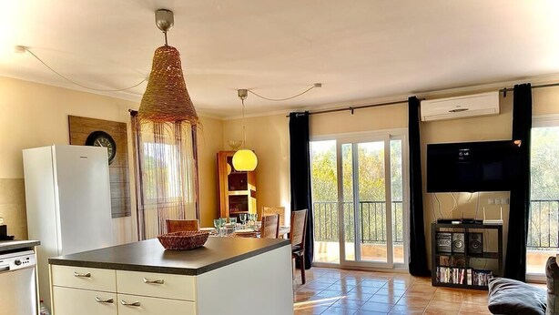 A kitchen with a central island, a dining area with a table and chairs, a TV, and a balcony with a view. - Has und Igel - Refuge in Cala Santanyi with Private Pool and Barbecue (Cala Santanyí)