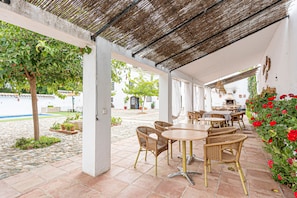 Eine Terrasse im Freien mit Korbmöbeln, einem Reetdach und Topfpflanzen.