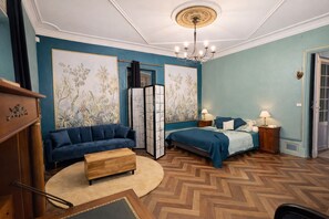 Une pièce comprenant un canapé, un lit, une table basse en bois, un paravent décoratif et un lustre.