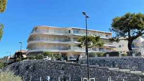 A multi-story building with balconies, a stone retaining wall, and a clear blue sky. - 50 m from the beach - Beautiful garden apartment in a charming building (Antibes)