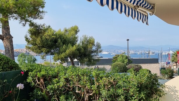 A coastal view with a marina, trees, and a clear sky. - 50 m from the beach - Beautiful garden apartment in a charming building (Antibes)