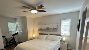 A bedroom with a bed, a ceiling fan, a window, a nightstand, and a bicycle. - Charming 2-bedroom Stratton Mountain Condo with shuttle service (Stratton)