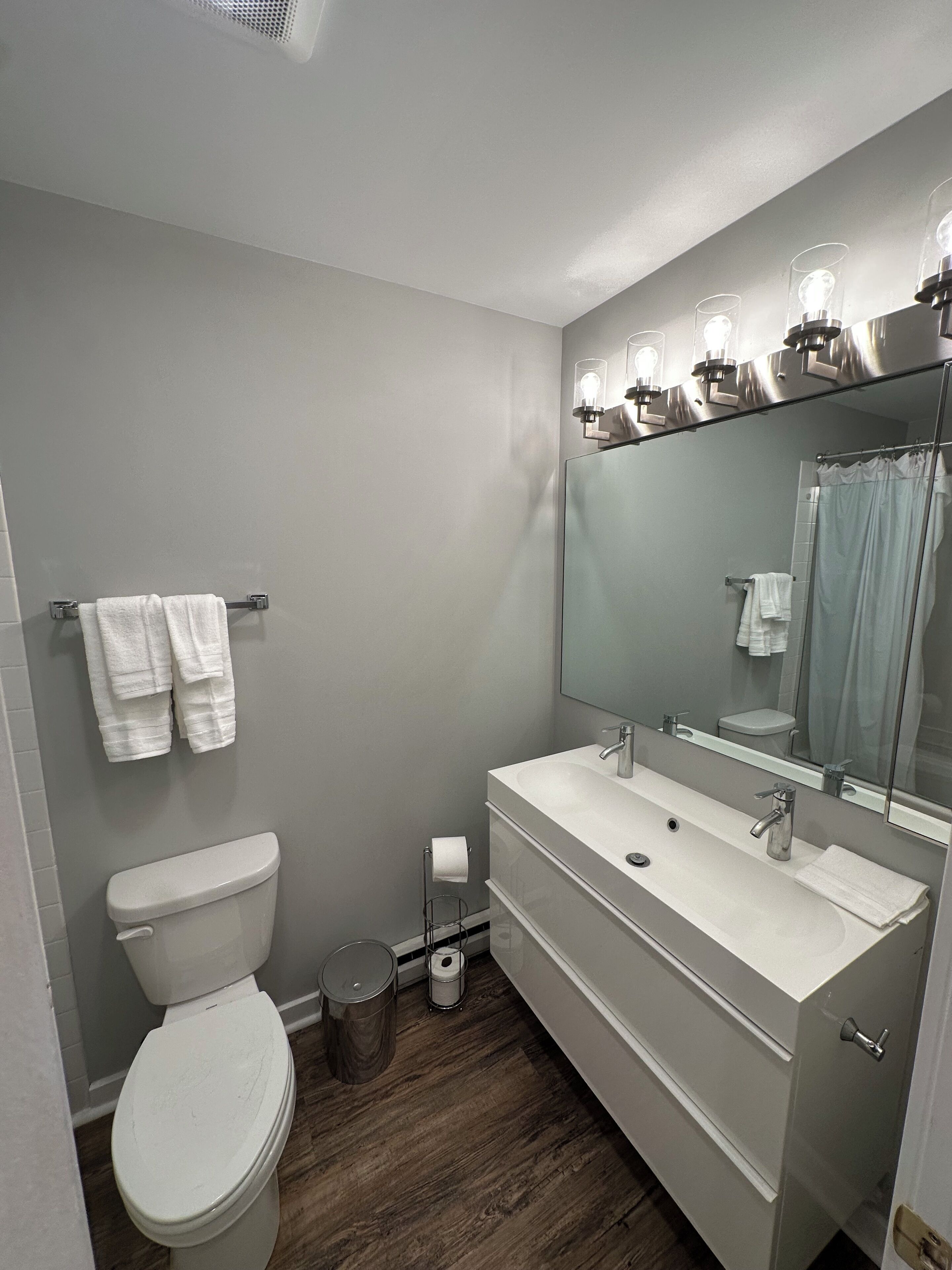 Een moderne badkamer met een wit toilet, een grote spiegel en een wastafelmeubel met een wastafel.