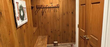 Un pasillo revestido de madera con un banco, un perchero y una puerta.