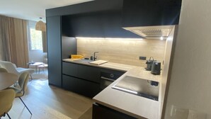 A modern kitchen with a built-in stove, a sink, and a coffee machine. There is a dining area with a table and chairs. - Appt Prestige - accès facile piste - Thalasso (Saint-Lary-Soulan)