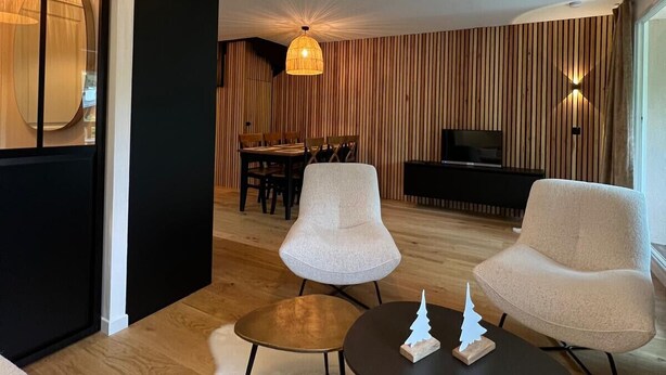 A modern living room with two white armchairs, a round coffee table, and a large, textured ceiling light. - Appt Prestige - accès facile piste - Thalasso (Saint-Lary-Soulan)