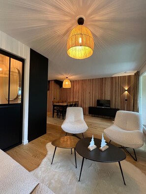 Uma sala de estar moderna com dois poltronas brancas, uma mesa de centro redonda e uma luminária de teto grande e texturizada.