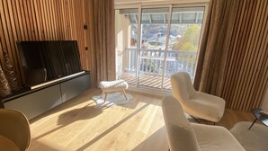 A modern living room with a flat-screen TV, a white fluffy ottoman, and a beige sofa. - Appt Prestige - accès facile piste - Thalasso (Saint-Lary-Soulan)