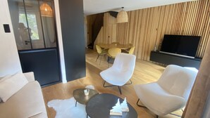 A modern living room with a sofa, two armchairs, a coffee table, and a dining area with a table and chairs. A flat-screen TV is mounted on the wall. - Appt Prestige - accès facile piste - Thalasso (Saint-Lary-Soulan)