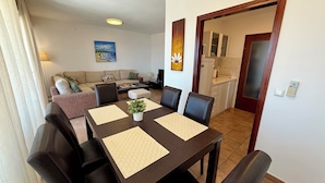 A dining area with a table set for four, a sofa, a TV, and a kitchen in the background. - Apartment Val (Crikvenica)