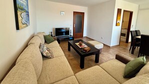 A living room with a sofa, a coffee table, a TV, and a painting on the wall. - Apartment Val (Crikvenica)