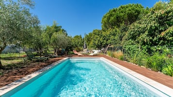 A rectangular swimming pool with clear blue water, surrounded by a wooden deck and greenery.