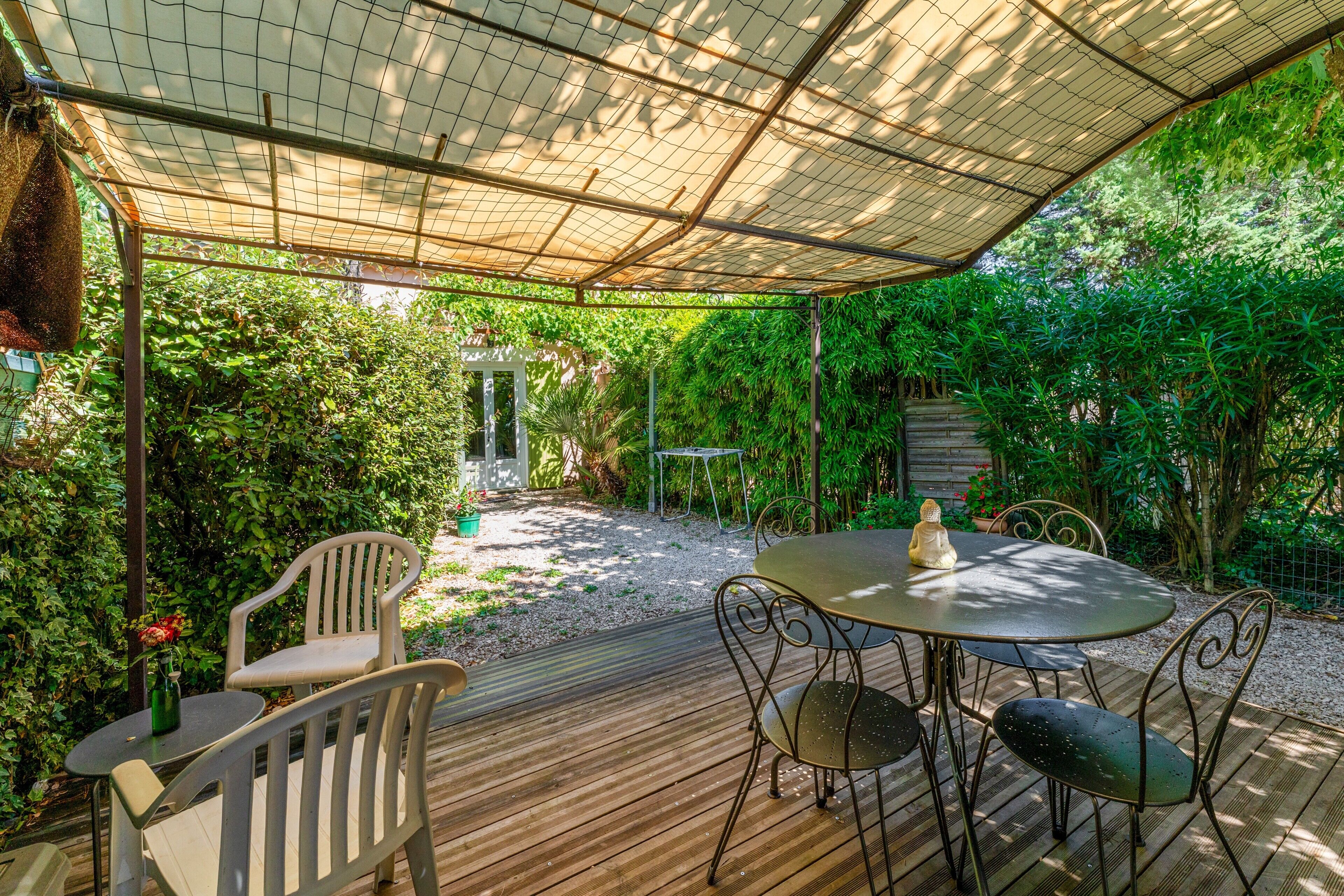An outdoor patio with a table and chairs, surrounded by greenery and a covered area.