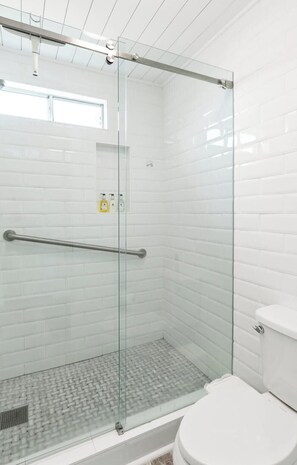 A modern bathroom with a glass-enclosed shower, white tiled walls, and a white toilet.