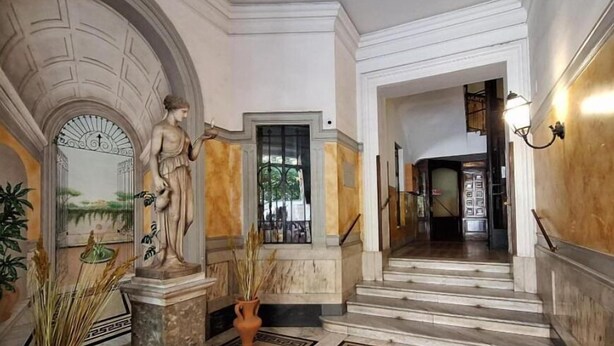 A grand hallway with marble flooring, classical statues, and a staircase leading to another area. - HEBE Eternity Rooms (Rome)