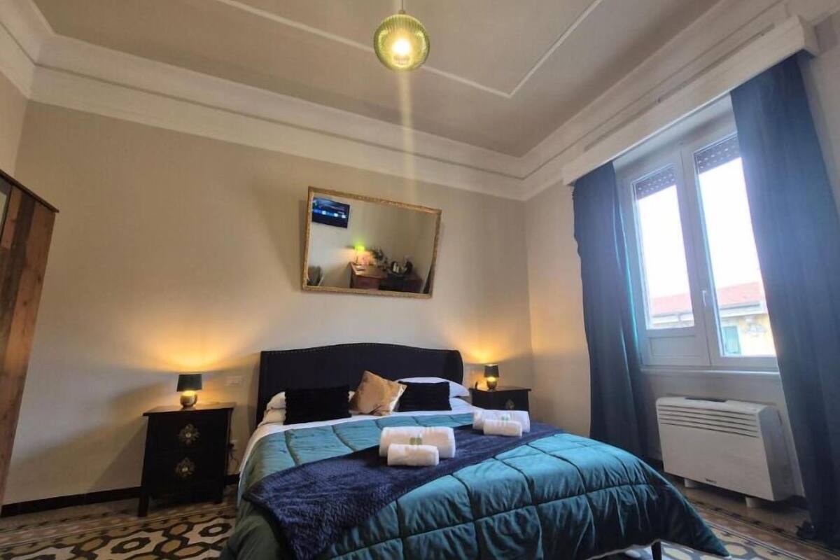 A hotel room with a bed, a nightstand, a mirror, and a window with curtains.