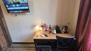 A hotel room with a TV mounted on the wall displaying various channels, a wooden desk with a lamp, a bottle of wine, and a remote control. - HEBE Eternity Rooms (Rome)
