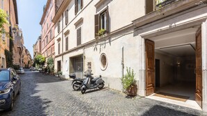 A cobblestone street with a parked scooter, a building with a wooden door, and a parked car.