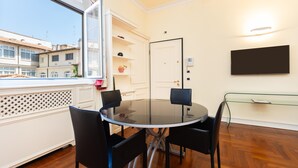 A dining area with a round glass table, black chairs, a white door, and a TV mounted on the wall.