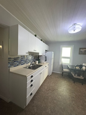 A compact kitchen with white cabinets, a built-in microwave, and a sink. There's a dining area with a table and chairs.