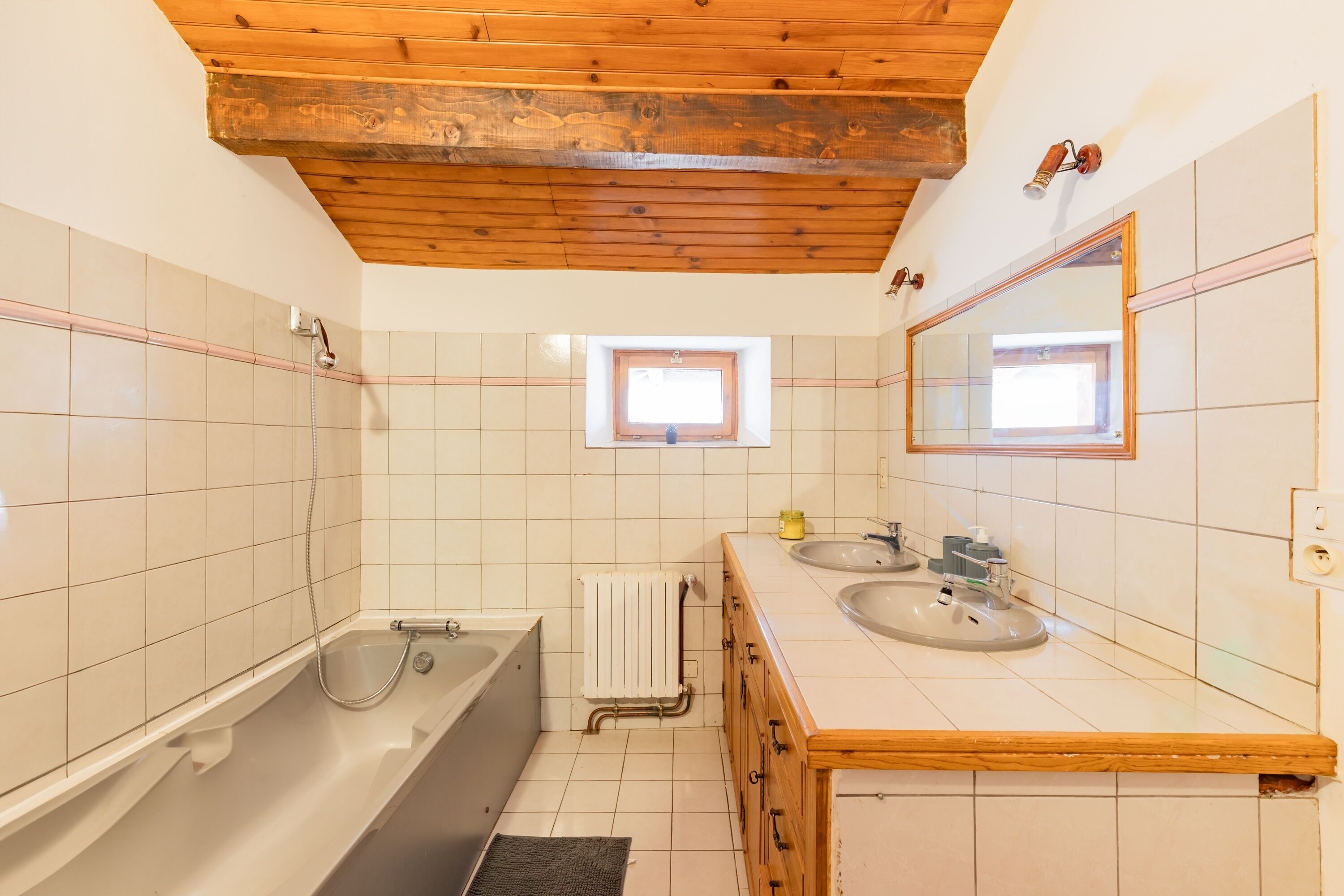Un bagno con soffitto in legno, una vasca, una finestra e due lavandini.