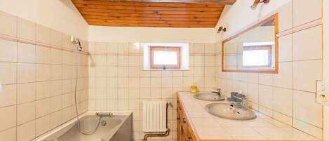 Un bagno con soffitto in legno, una vasca, una finestra e due lavandini.