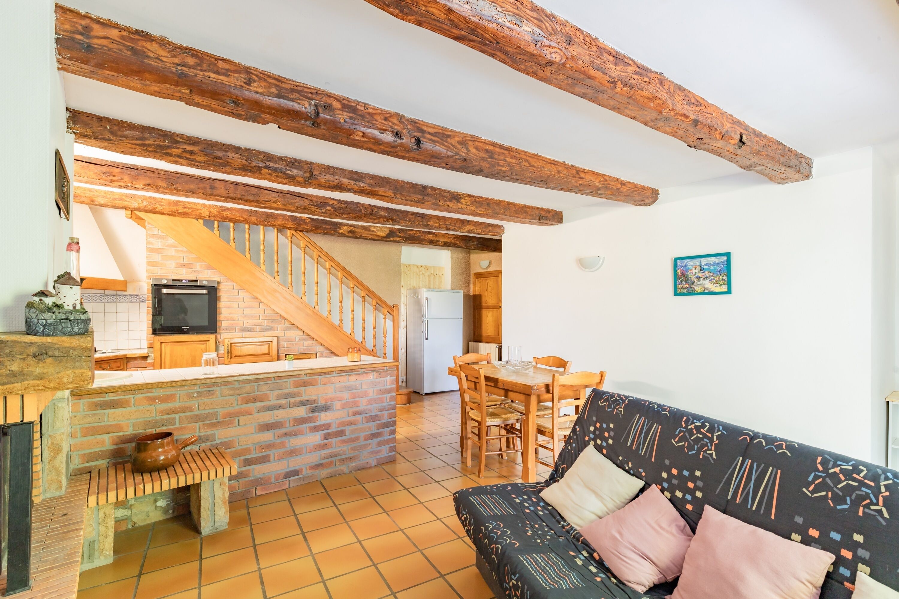 Ein gemütlicher Wohnbereich mit freiliegenden Holzbalken, einem Kamin aus Ziegeln, einer Couch und einem Esstisch.