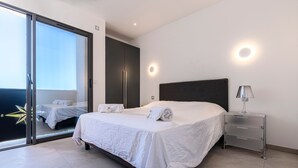 Een moderne slaapkamer met een groot bed, een nachtkastje, een schuifdeur naar een balkon en een wandlamp.