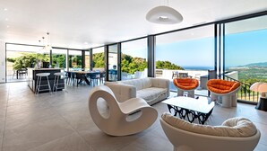 Een ruime zithoek met een moderne witte bank, een bijzondere witte fauteuil en oranje armstoelen. In de achtergrond staat een eettafel met stoelen.