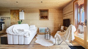 Ein gemütliches Blockhaus-Interieur mit Holzausbau, einem weißen Sofa, einem Sessel, einem kleinen Tisch und einem Fernseher.
